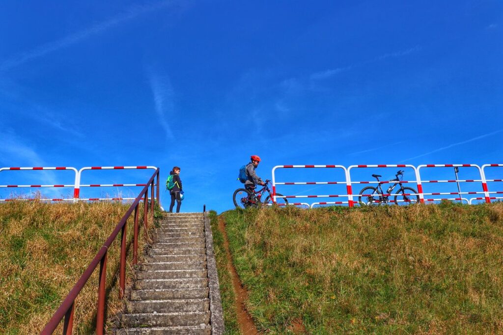 Dębno, strome schody prowadzące na szlak rowerowy Velo Czorsztyn, rowerzyści - dziecko, mężczyzna, niebieskie niebo
