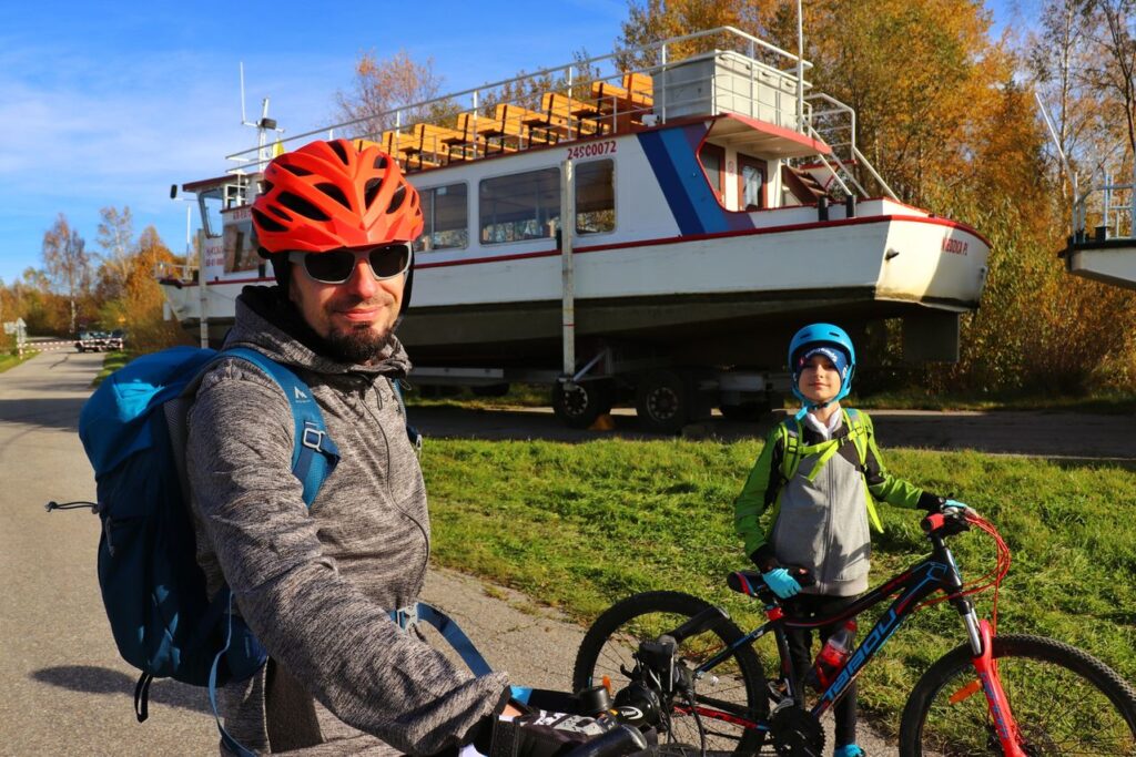 Uśmiechnięci rowerzyści - dziecko z tatą na tle statku wycieczkowego nad Jeziorem Czorsztyńskim 