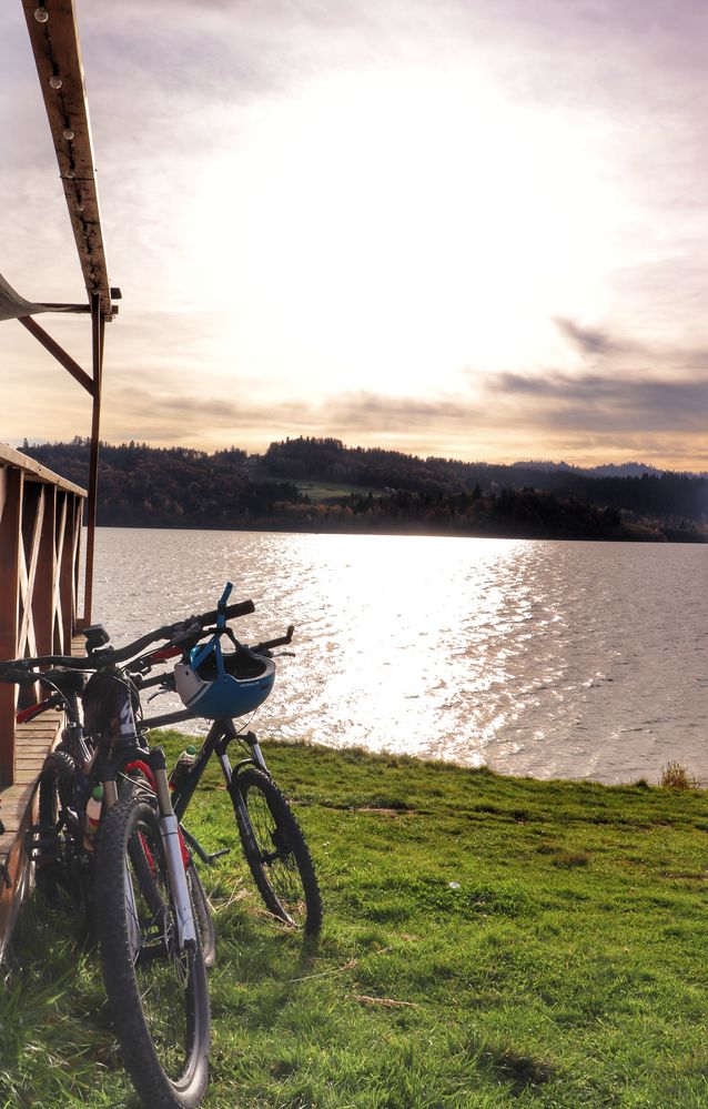 Rowery oparte o drewniany taras baru Fabryka Smaku na trasie rowerowej Velo Czorsztyn, widok na Jezioro Czorsztyńskie