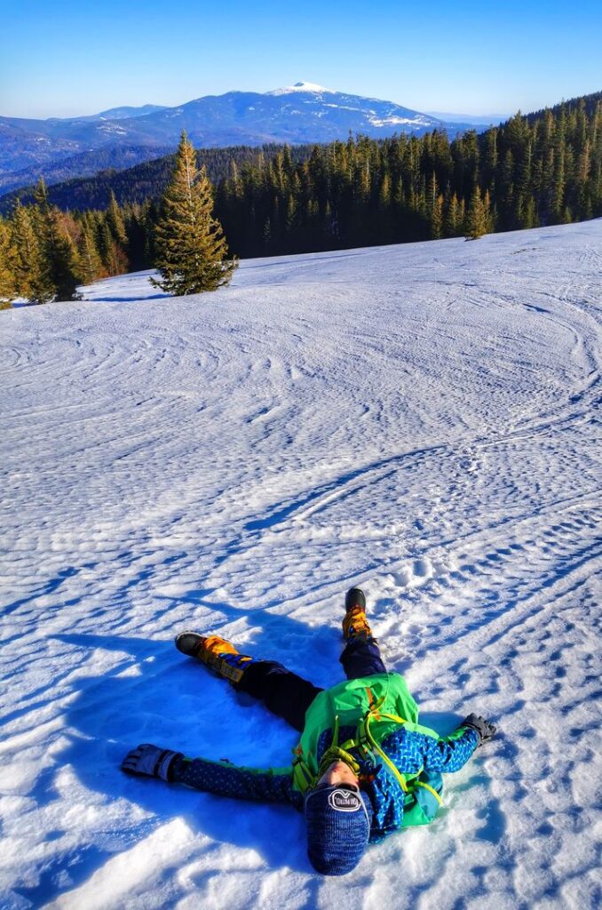 Hala Jodłowcowa zimą, dziecko leżące na śniegu, w tle widok na Babią Górę
