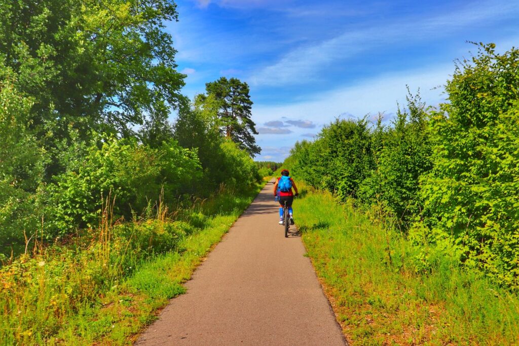 Prosta, asfaltowa droga na trasie rowerowej Rowerem po Kolei na Mazurach, rowerzysta, letnie popołudnie