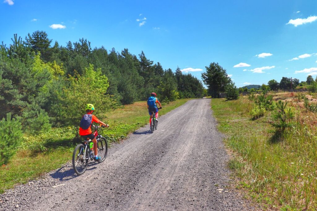 Rowerzyści - dziecko z tatą na czerwonym rowerowym Szlaku Orlich Gniazd, droga szutrowa 