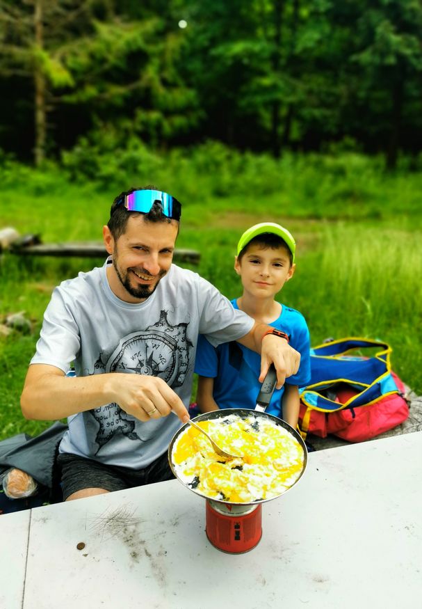 Szczęśliwy turysta z dzieckiem robiący jajecznicę na butli gazowej na szczycie Palenica w Beskidzie Śląskim, letnie popołudnie