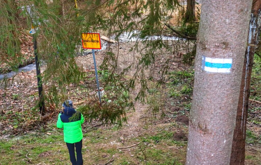 Turysta na niebieskim szlaku idącym z Jaworzynki, las, tablica z napisem GRANICA PAŃSTWA