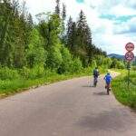 Szeroka droga asfaltowa prowadząca do Jaworzynki, dziecko z tatą na rowerze