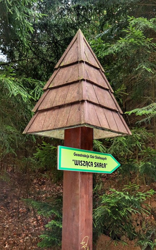 Drewniany słup z daszkiem, zielona tabliczka z napisem - Geoatrakicje Gór Stołowych, Wisząca Skała