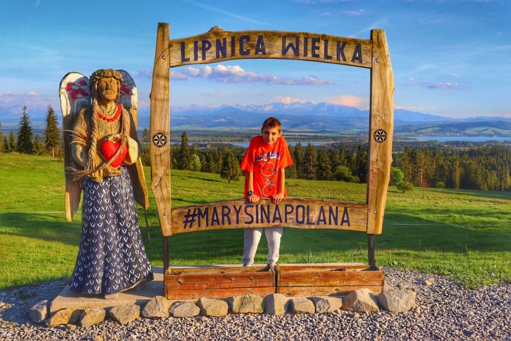 Lipnica Wielka - Marysina Polana, dziecko, drewniana ramka i rzeźba, w tle Tatry i Jezioro Orawskie