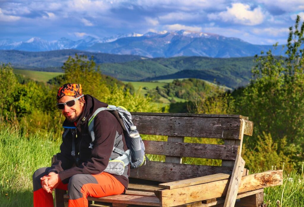 Uśmiechnięty turysta odpoczywający na ławce z palet na pięknej polanie na czerwonym szlaku na Magurkę na Słowacji, w tle Tatry