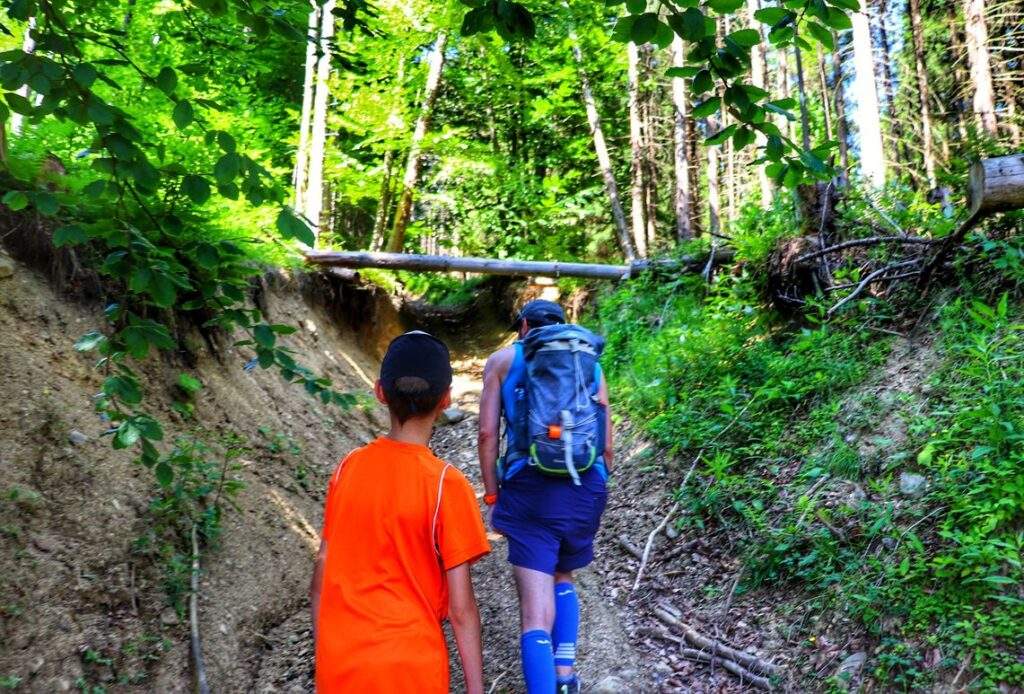 Dziecko z tatą, strome podejście przez las, letni dzień