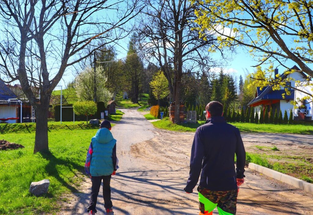 Turysta z dzieckiem, ścieżka prowadząca między zabudowaniami, Zakamenne
