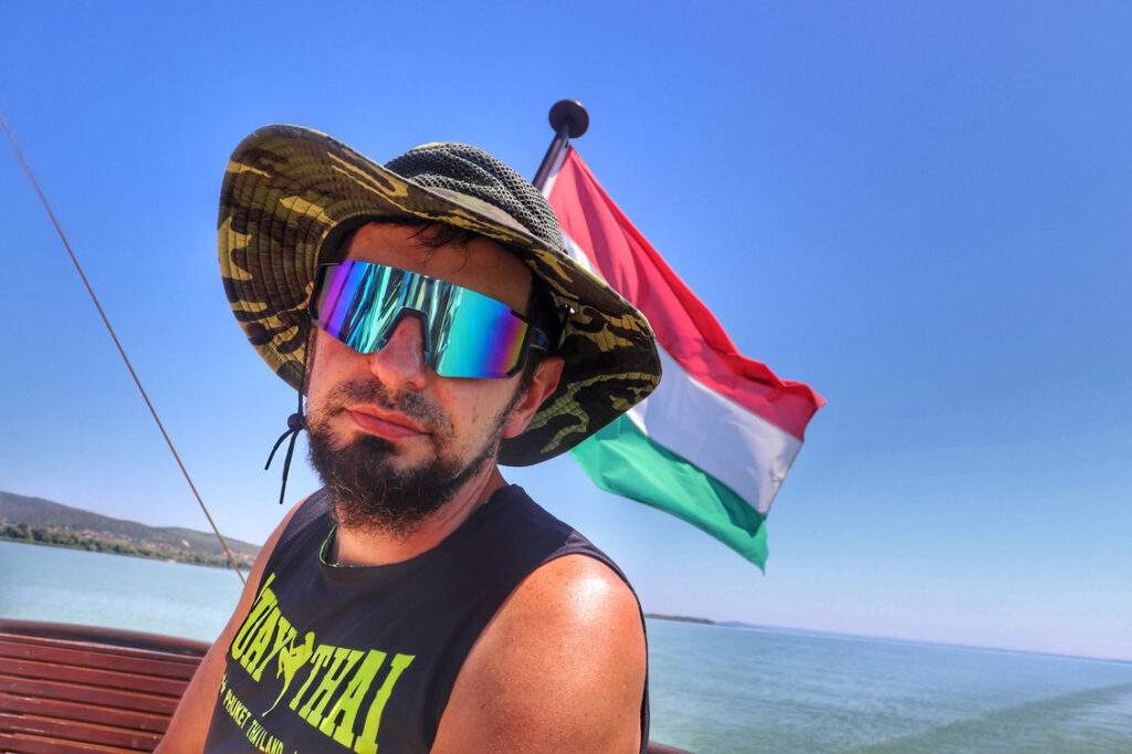 Turysta na statku wycieczkowym, w tle węgierska flaga, drewniane ławki, widok na Balaton