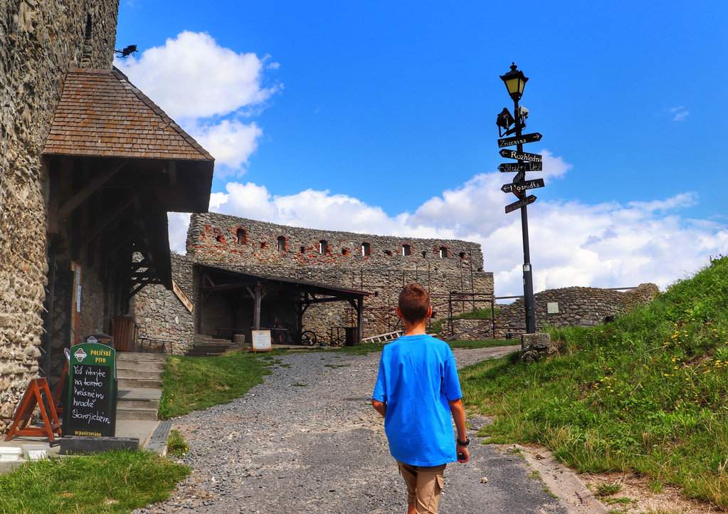 Dziecko, szeroka droga asfaltowa, Zamek Stary Jiczyn, restauracja, latarnia, drogowskazy, letni dzień