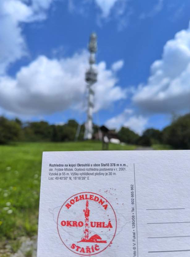 Pocztówka z pieczątką wieży widokowej na wzgórzu Okrouhlá w Czechach, w tle wieża widokowa, niebieskie niebo, białe chmury