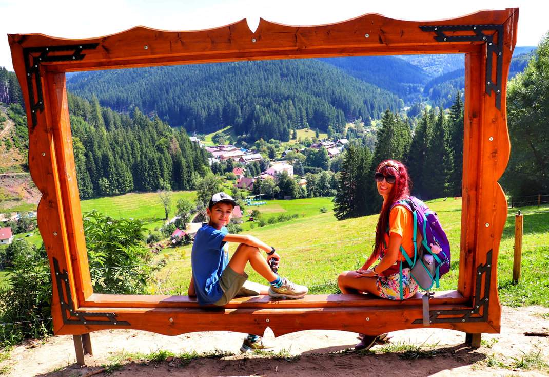 Dziecko z mamą przy dużej drewnianej ramce na zielonym szlaku prowadzącym do wieży widokowej Miloňová w Czechach - Ścieżka Valachy (Fotostezka Valachy)