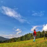 Turysta z dzieckiem wędrujący w górę polany, w tle górski krajobraz i niebieskie niebo - trasa poza szlakiem, Rycerka Górna