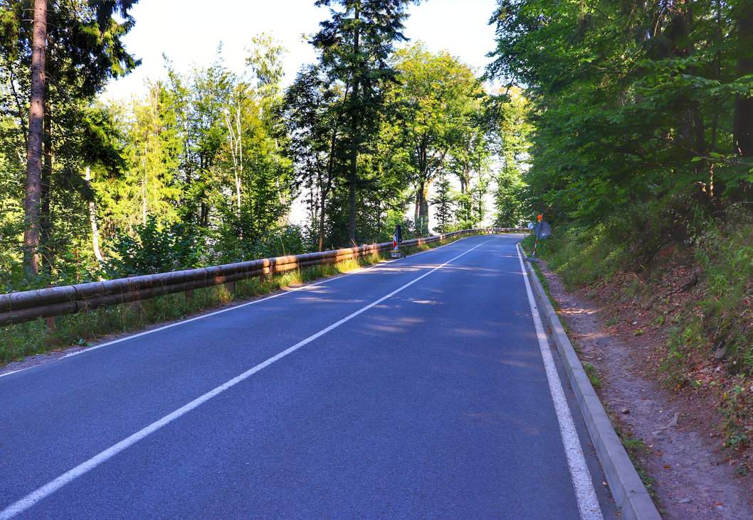 Szeroka asfaltowa droga na zielonym szlaku turystycznym prowadzącym do ruin zamku Oheb