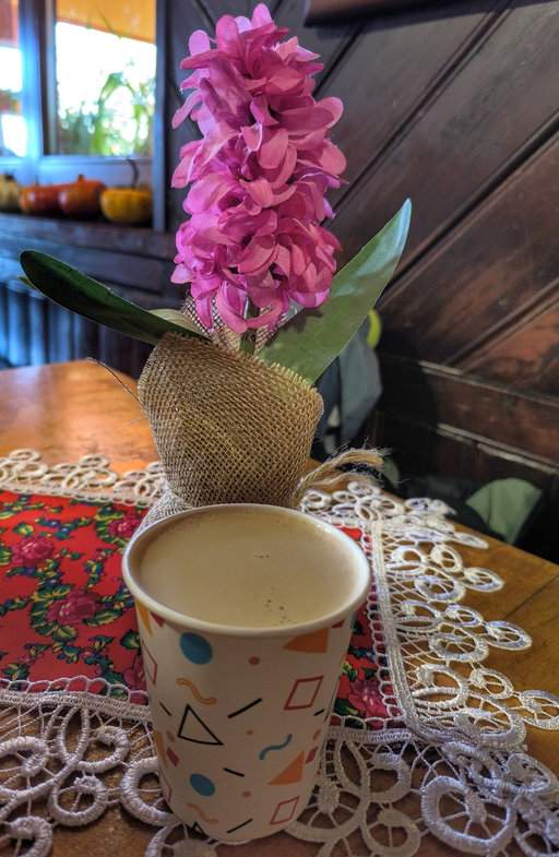 Wnętrze schroniska na Leskowcu - drewniany stół z serwetką, kubkiem aromatycznej kawy z ekspresu i kwiatem, który dodaje wnętrzu przytulnego klimatu