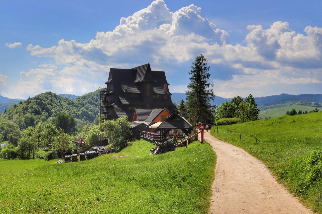 Szeroka, utwardzona droga z widokiem na budynek Schroniska PTTK Trzy Korony, lato