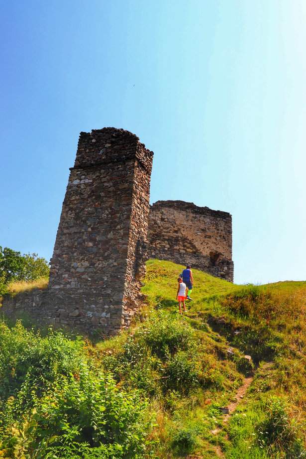 Turysta z dzieckiem wspinający się stromą ścieżką w kierunku ruin zamku Brníčko w Czechach, w piękny, słoneczny, letni dzień