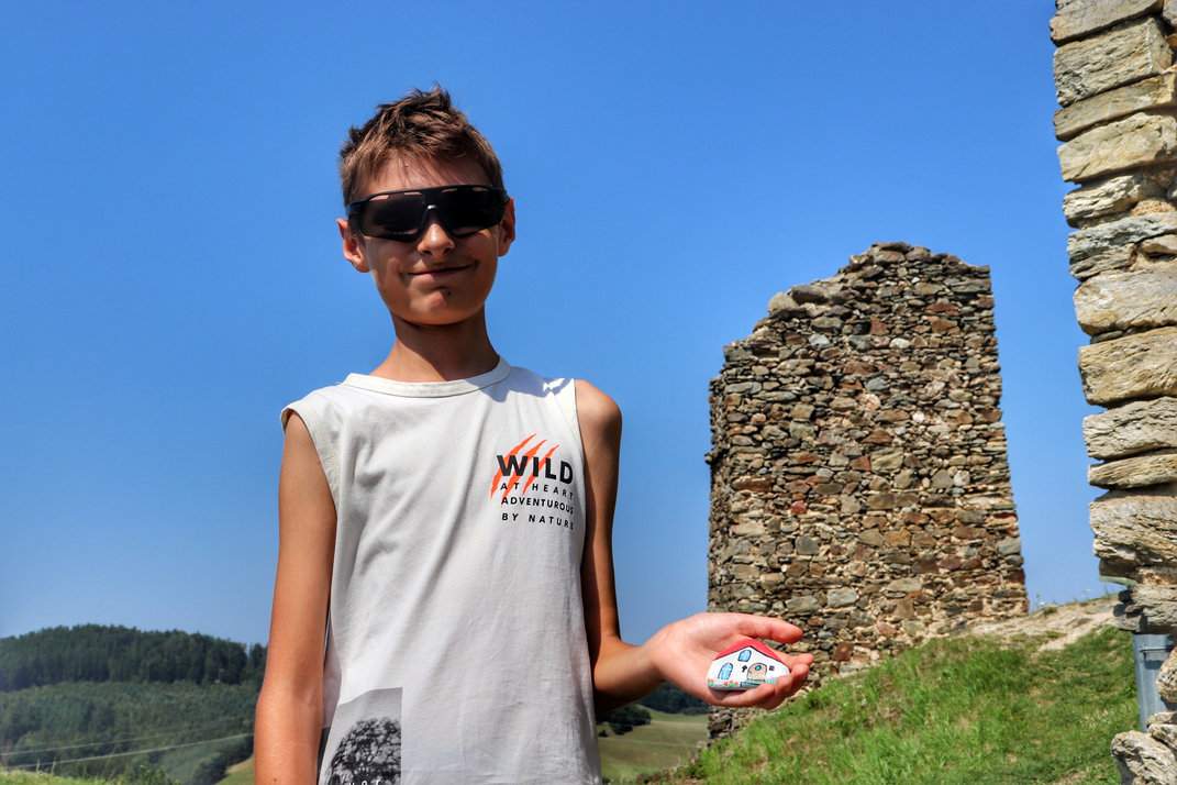 Radosne dziecko trzymające kamyk, na tle malowniczych ruin zamku Brníčko w Czechach