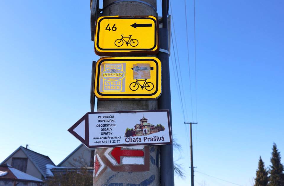 Słup z białą tabliczką wskazującą kierunek do Chaty Prašivá, oznaczeniem czerwonego szlaku oraz żółtymi tabliczkami szlaku rowerowego