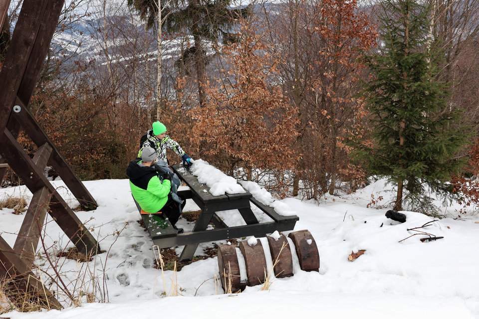 Turysta z dzieckiem siedzący przy drewnianym, pokrytym śniegiem stole przy schronie turystycznym na słowackim szlaku