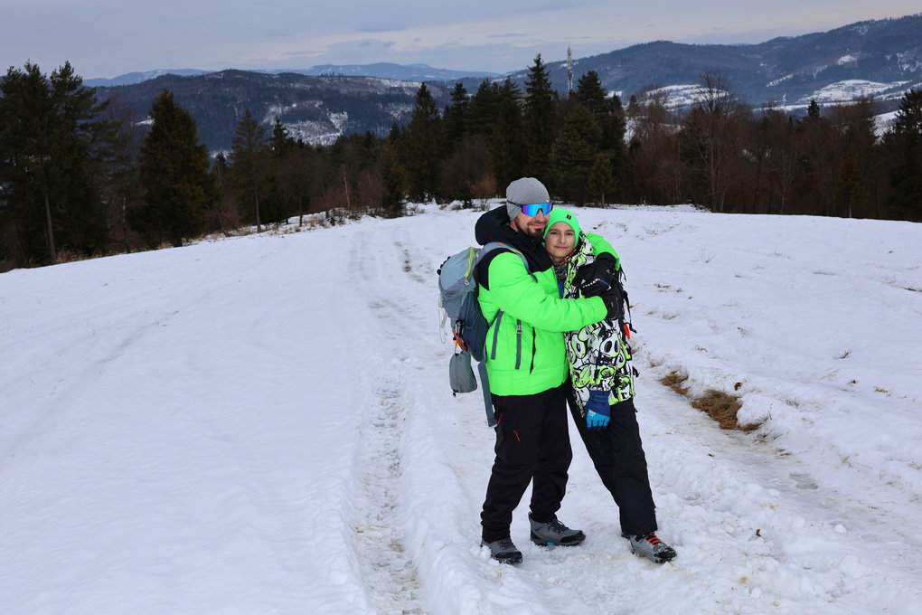 Turysta przytulający dziecko na szlaku na Gładki Wierch (Hladký vrch) na Słowacji, na zaśnieżonej polanie, w tle górski krajobraz