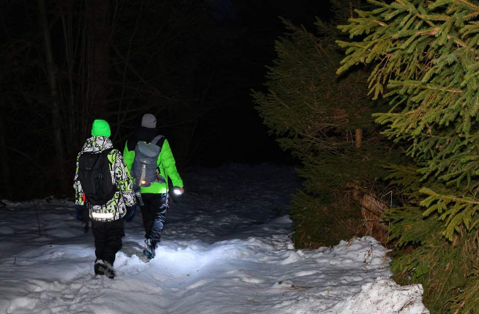 Dziecko z tatą oświetlający zimową leśną ścieżkę latarką - późny wieczór na słowackim szlaku