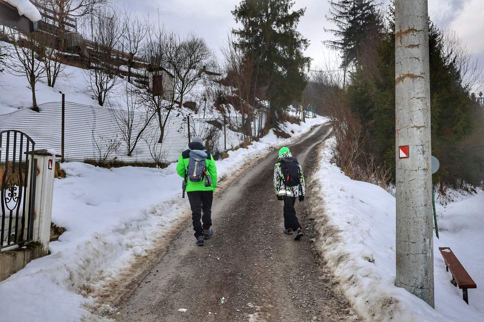 Turysta z dzieckiem idący w górę asfaltowej drogi oznaczonej czerwonymi znakami - Krásno nad Kysucou, Słowacja 