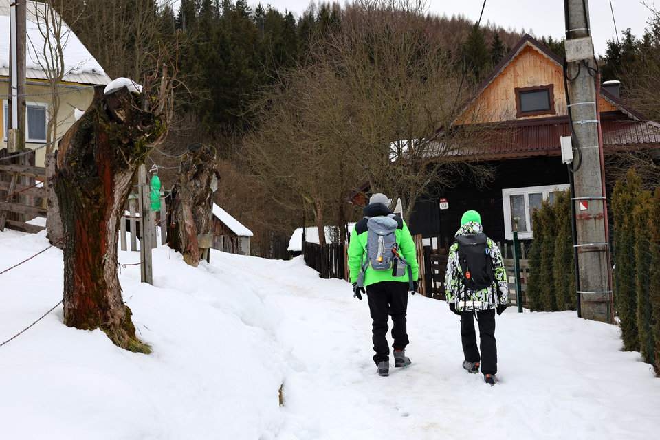 Turysta z dzieckiem idący w górę zaśnieżonej drogi między domami - Krásno nad Kysucou, Słowacja