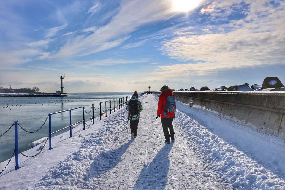 Spacer turysty z dzieckiem po zachodnim falochronie w Helu podczas pięknego, słonecznego zimowego dnia