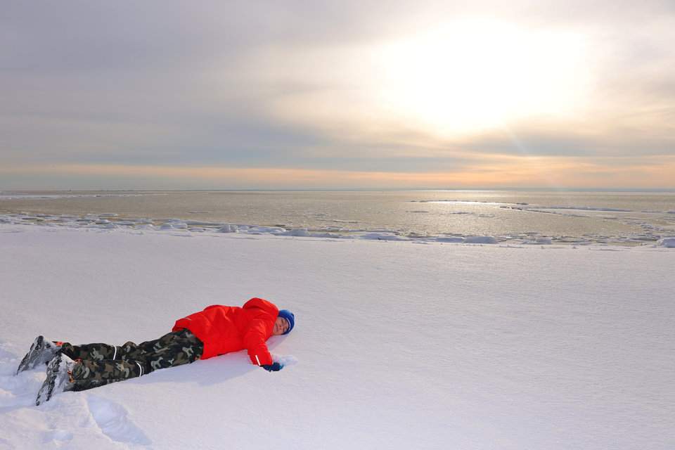 Dziecko leżące na zaśnieżonej plaży, z niebem cudownie rozświetlonym zimowym słońcem