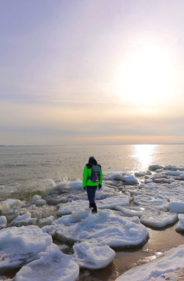 Turysta na plaży w Helu przy zimowym zachodzie słońca, nad zmrożonym brzegiem Bałtyku