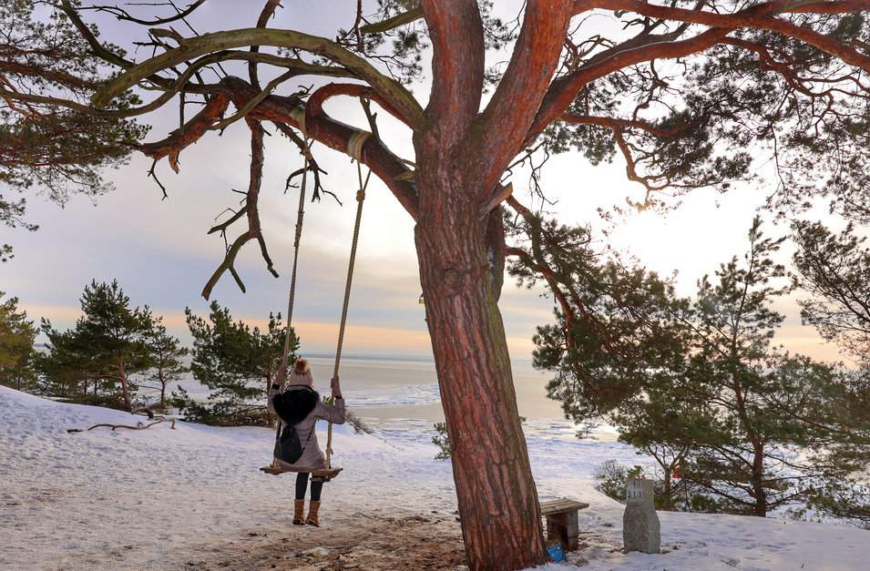 Kobieta podziwiająca zachód słońca siedząca na huśtawce na plaży w Helu, widok na Morze Bałtyckie