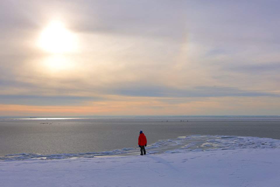 Helska plaża zimą o zachodzie słońca, z dzieckiem stojącym nad brzegiem zmrożonego Morza Bałtyckiego
