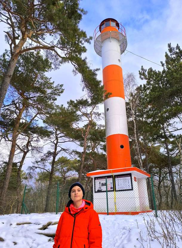 Jastarnia, Półwysep Helski - uśmiechnięte dziecko na tle charakterystycznej biało-czerwonej latarni morskiej w lesie