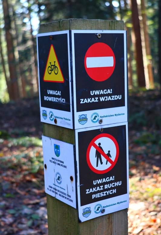 Słup z ostrzeżeniami o trasie rowerowej Rodzinny Flow, która przecina zielony szlak na Chełm w Beskidzie Wyspowym